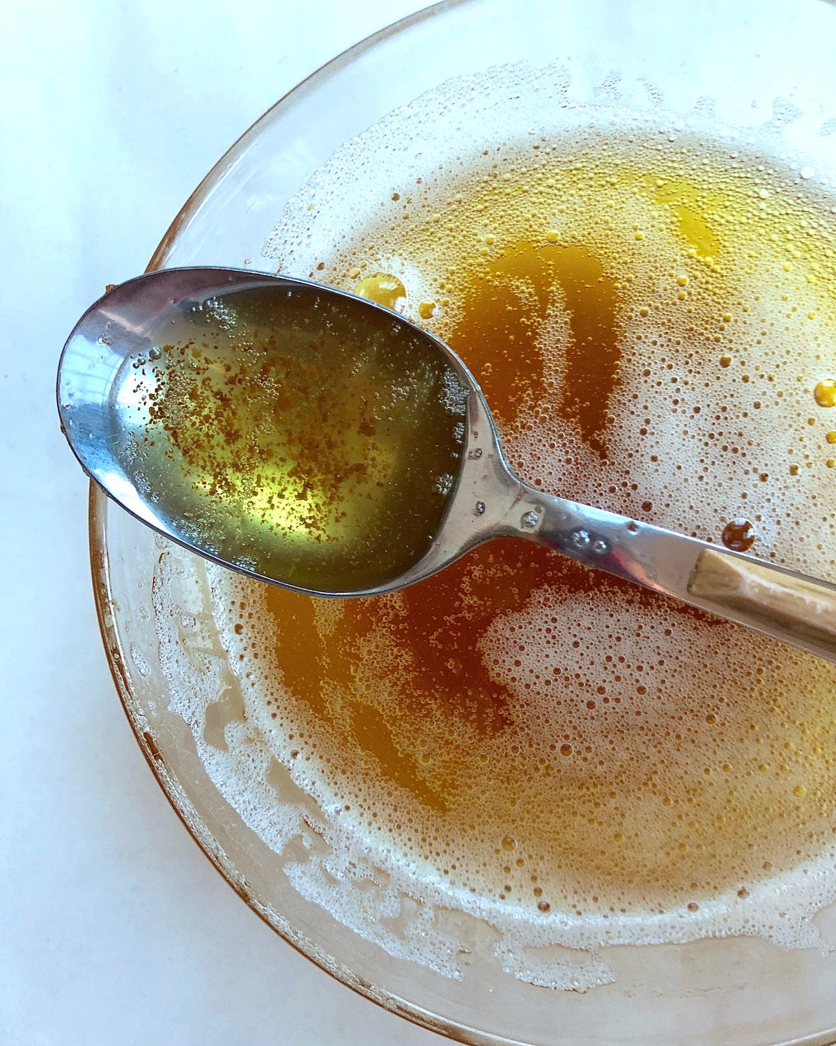 Brown butter in a bowl with some in a spoon showing the darker milk solids under the liquid fat.